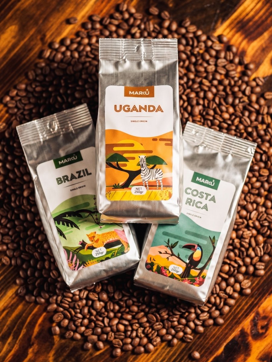 Marcus Coffee Shop bags of Brazil, Uganda, and Costa Rica single-origin coffee, surrounded by roasted beans